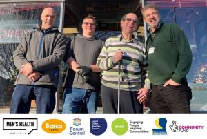 4 men stand smiling together outside a barber shop. Mens Health Unlocked partner logos at the bottom.