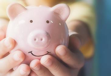 Image shows a young person holding a piggy bank.