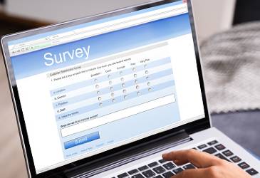 Image shows a persons hand on a laptop,, completing a survey.