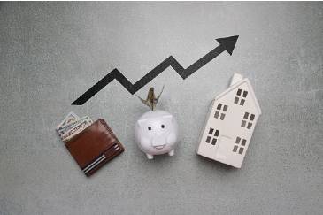 Image shows a wallet, piggy bank and a house in a row. Behind them is a line from a graph pointing up.