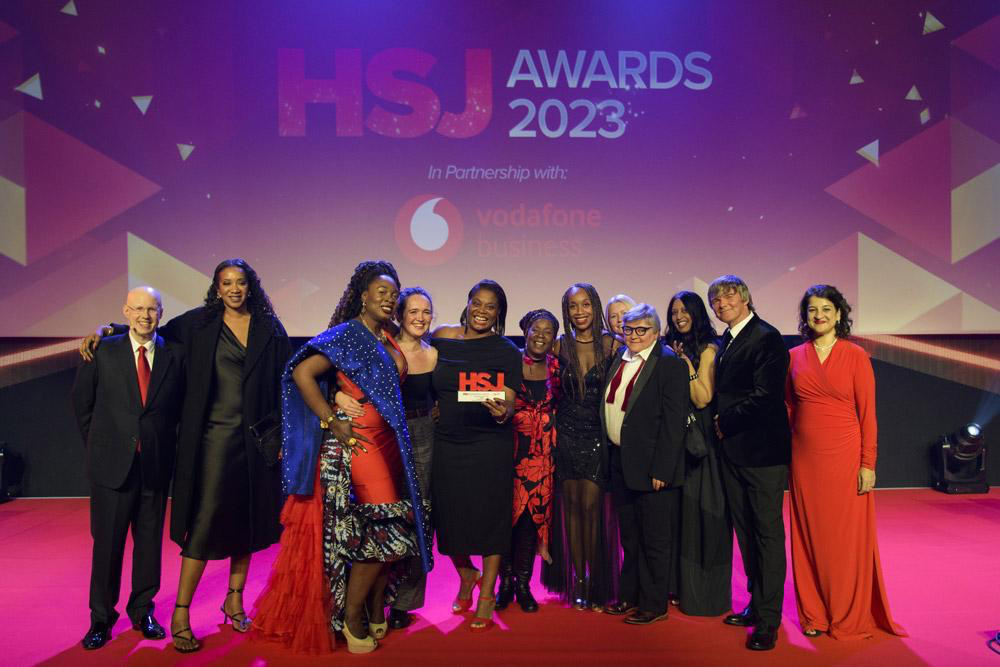 Photo shows the Synergi-leeds team at the HSJ Awards. They are stood on stage, smiling at the camera holding an award that says 'HSJ Mental Health Innovation of the Year Award 2023'.