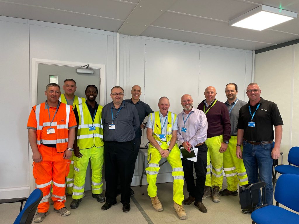 10 men, some in hi visibilty constriction workwear stand for a photo